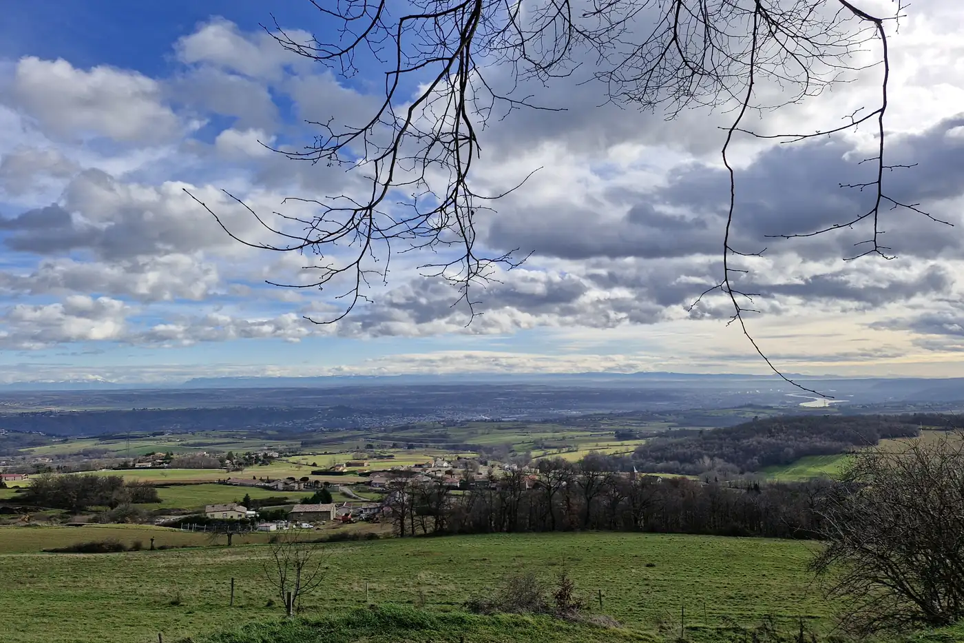 Vue sur la plaine depuis les hauteurs du Pilat, en hiver, cadrée par des branches nues.